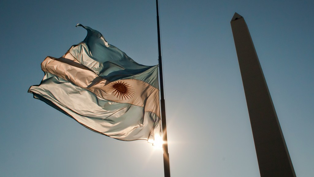 Bandeira da Argentina e Obelisco contra o sol, na Avenida 9 de Julio, em Buenos Aires