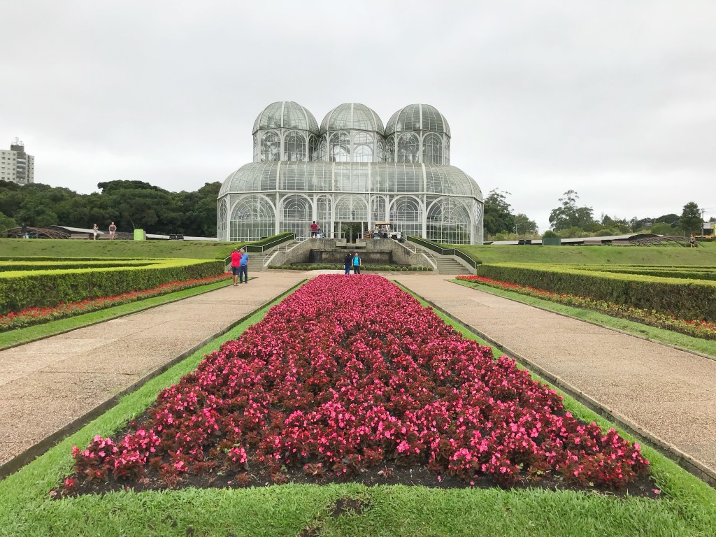 A imagem mostra a estufa principal do Jardim Botânico. Ela parece um castelo com três cúpulas de vidro