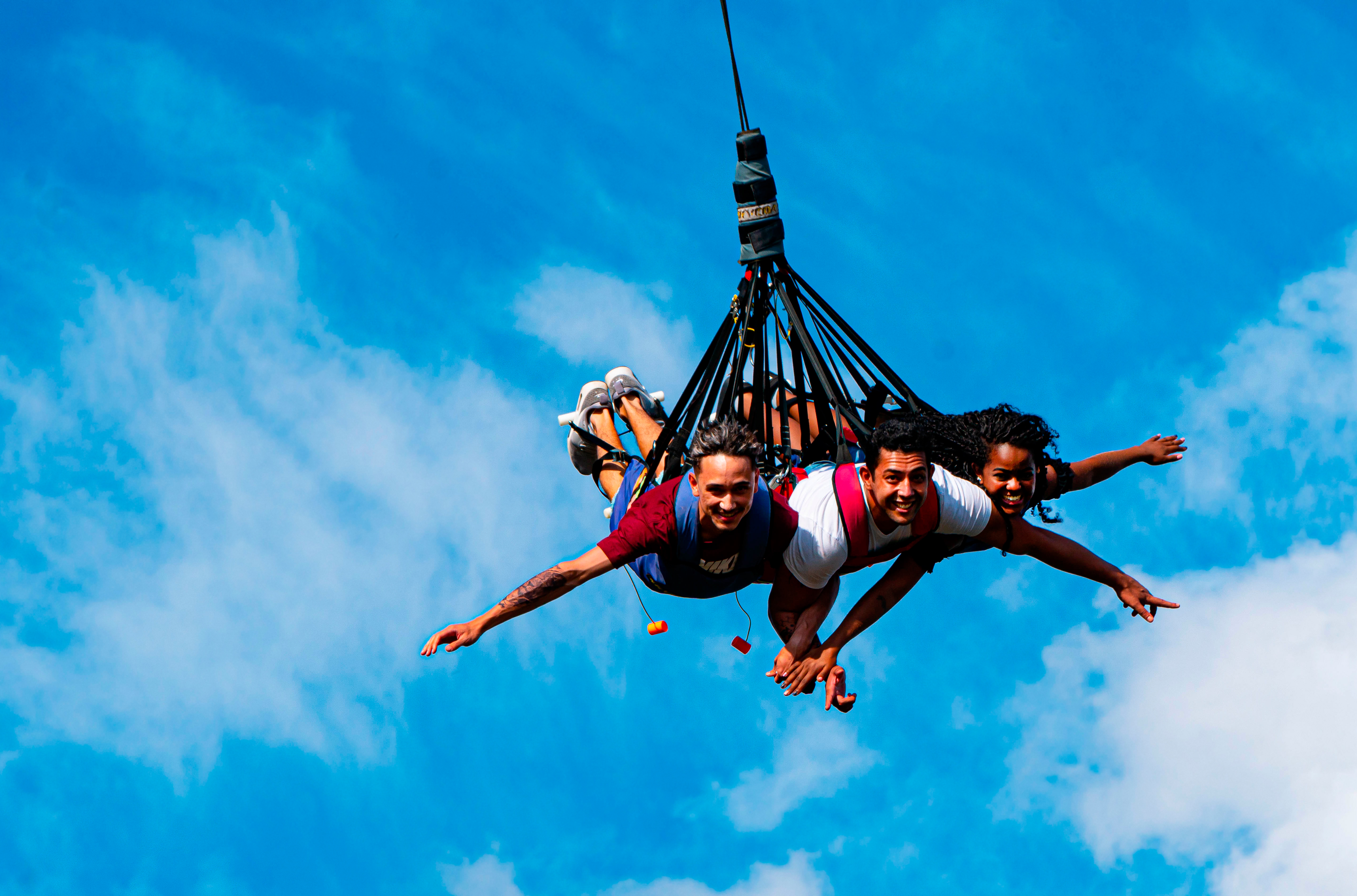 A imagem mostra três pessoas fazendo uma espécie de voo penduradas por um cabo