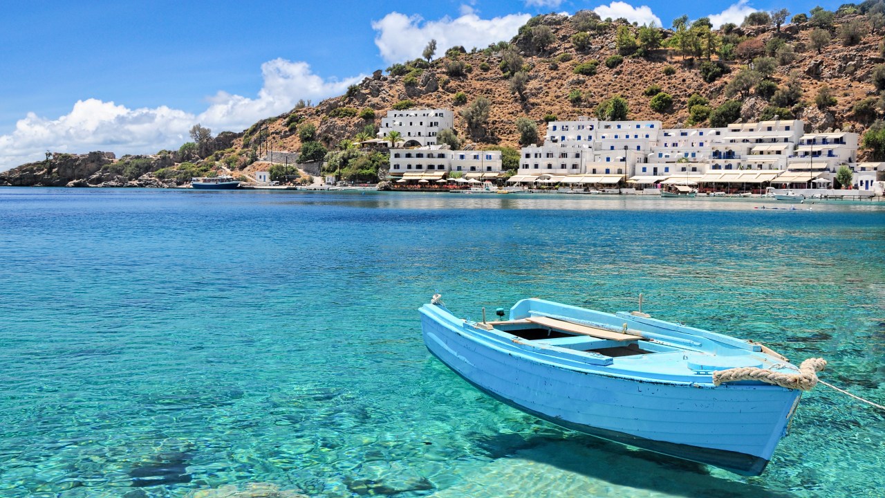Barco no mar com a aldeia de Loutro em Creta, ilha da Grécia, ao fundo