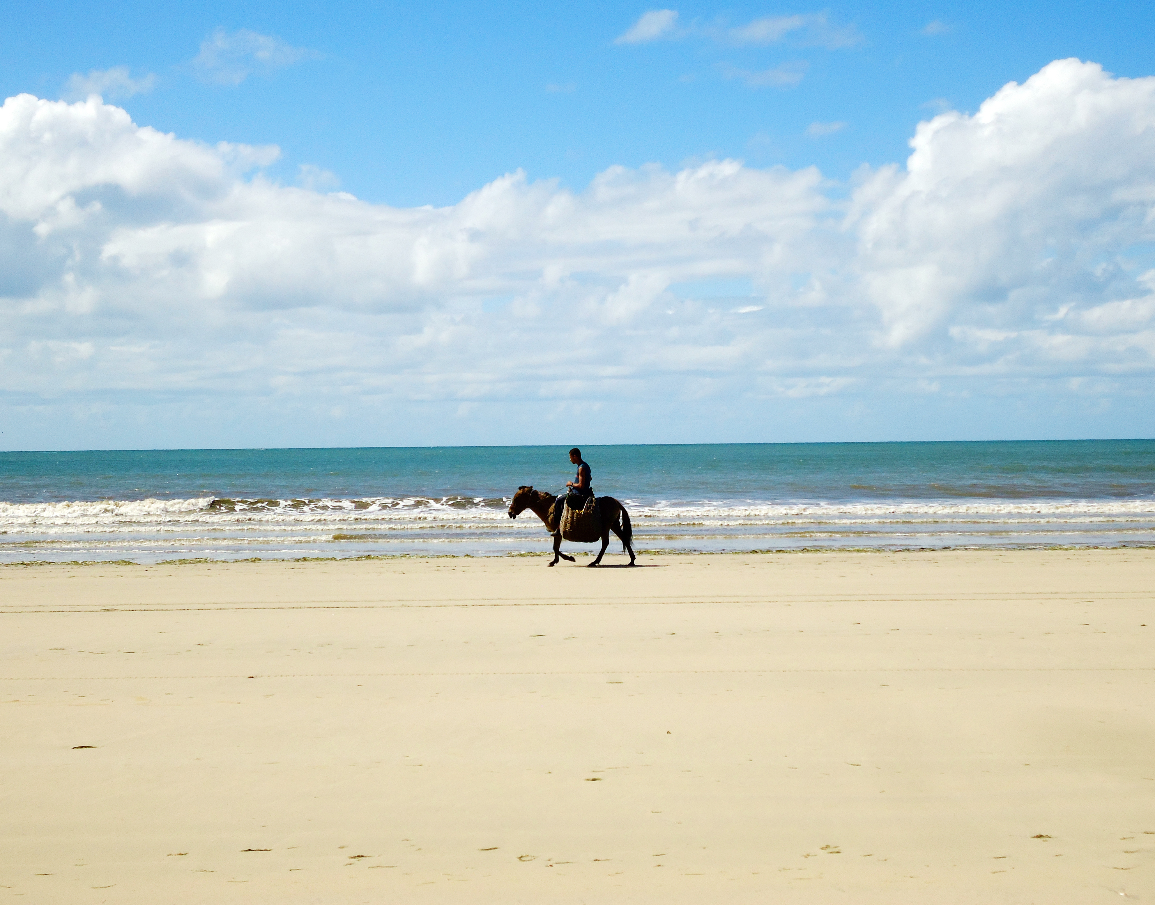 Homem passeia a cavalo na praia deserta de Bainema, na Bahia