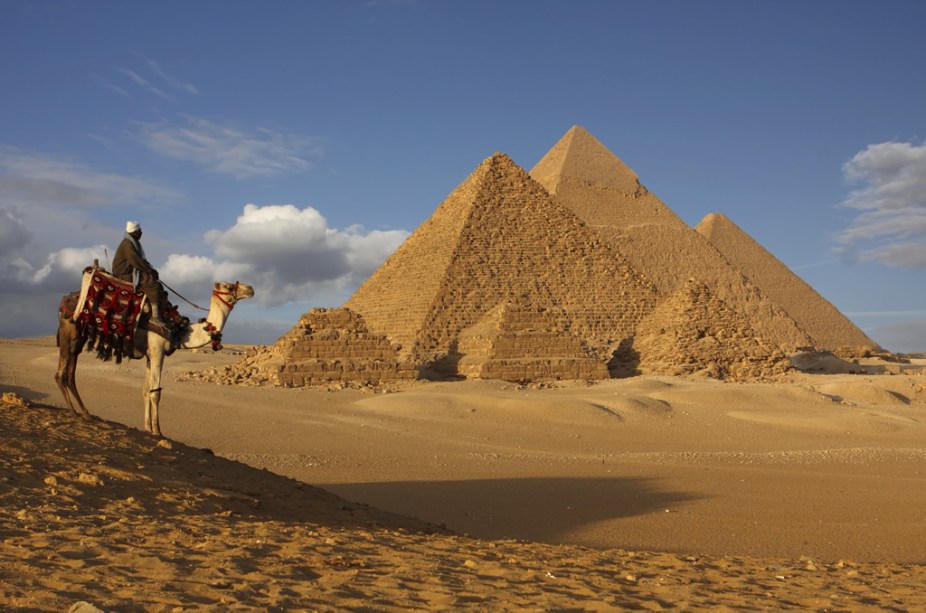 Beduíno e dromedário no platô de Gizé. Ao visitante, atenção, as pirâmides estão coladas aos subúrbios da <a href="https://viajeaqui.abril.com.br/cidades/egito-cairo" rel="cidade do Cairo" target="_blank">cidade do Cairo</a>, no <a href="https://viajeaqui.abril.com.br/paises/egito" rel="Egito" target="_blank">Egito</a>
