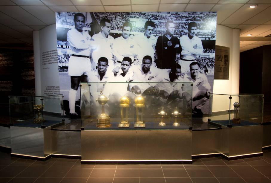 As taças dos títulos mundiais do Santos e, ao fundo, a foto do time campeão