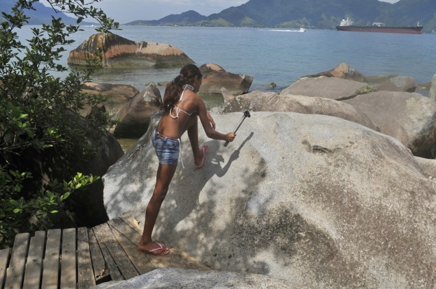 Turista bate o martelo para ouvir o som oco da <strong>Pedra do Sino</strong>, na Praia Garapocaia (ou Praia da Pedra do Sino)