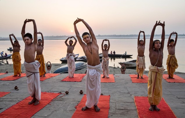 Jovens hindus praticam ioga na beira do rio Ganges, em Varanasi