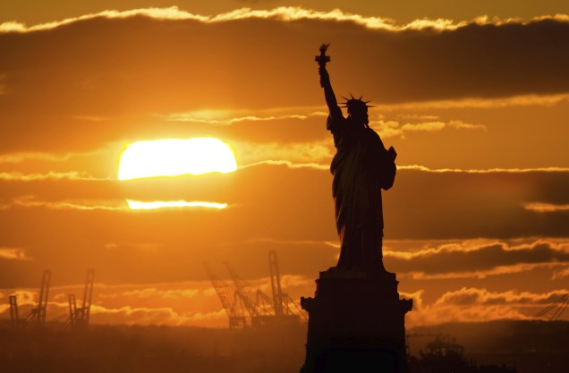 Pôr do sol em <a href="https://viajeaqui.abril.com.br/cidades/estados-unidos-nova-york" rel="Nova York" target="_blank">Nova York</a>, com a silhueta da <a href="https://viajeaqui.abril.com.br/estabelecimentos/estados-unidos-nova-york-atracao-estatua-da-liberdade-e-ellis-island" rel="Estátua da Liberdade" target="_blank">Estátua da Liberdade</a>