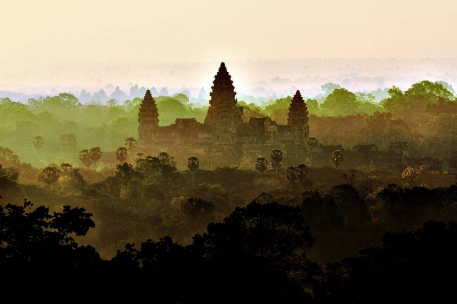 <strong>Angkor: uma imensidão de construções estonteantes</strong>Angkor se apresenta aos visitantes como um vasto território de floresta tropical com templos e pontes de pedra monumentais e maravilhosos no meio do caminho. Em seu auge, Angkor ocupava uma área maior do que a de Paris atual, e seus templos usaram muito mais pedras do que todas as estruturas egípcias juntas! Angkor Wat, na foto, é a maior estrutura religiosa do mundo