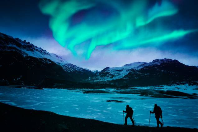 Alpinistas desbravando a Islândia, com as auroras boreais ao fundo