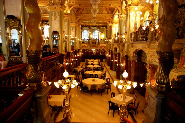 <strong>Cafe New York, Hungria</strong><br />    Foi inaugurado em outubro de 1894 como “o mais belo café do mundo". Seu interior esbanjava mármore, bronze, cristais, afrescos, luminárias e estofados em seda e veludo em estilo eclético que se aproximava do barroco. Ponto de encontro da elite húngara, ali se reuniam os círculos culturais e mundanos de <a href="https://viajeaqui.abril.com.br/cidades/hungria-budapeste" rel="Budapeste" target="_blank"><strong>Budapeste</strong></a>. Era o lugar perfeito para discutir ideias, saber as últimas novidades e, muito importante, ver e ser visto.<br />    <br />    Na década de 1910, além de seu público tradicional de intelectuais e jornalistas, foi ponto de encontro para cineastas como Alexander Korda, que então iniciava a sua carreira. A cidade chegou a ter 500 cafés entre 1910 e 1930. A deles maioria oferecia papel e tinta gratuitamente, além de um cardápio especial para escritores, a preço reduzido.<br />    <br />    Conta-se que o escritor húngaro Ferenc Molnár, que fazia da sua mesa no café seu local de trabalho, pretendendo que o mesmo ficasse aberto durante 24 horas, se apoderou da chave da porta e jogou-a no Danúbio para que nunca fosse fechada. Grande parte desses locais foi destruída durante a Segunda Guerra, outros não sobreviveram ao regime comunista e às crises financeiras. A partir de 2006, inteiramente restaurado e com muitas peças autênticas recuperadas, o <a href="https://viajeaqui.abril.com.br/estabelecimentos/hungria-budapeste-restaurante-cafe-new-york" rel="Café New York" target="_blank"><strong>Cafe New York</strong></a> voltou a ostentar o luxo e o brilho de outros tempos