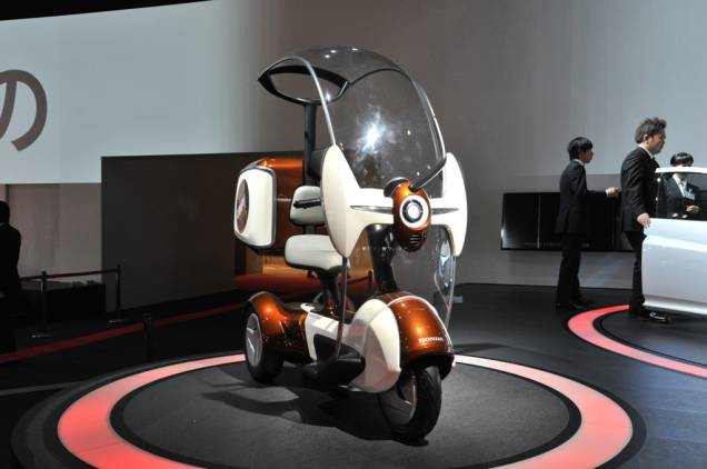 O E-canopy é o conceito da Honda para mobilidade urbana baseado em energias limpas. O scooter de três rodas possui protetor de chuva e pode vir equipado com bagageiro, o que pode ser uma excelente solução para o transporte de pequenas cargas para os motoboys O E-canopy é o conceito da Honda para mobilidade urbana baseado em energias limpas. O scooter de três rodas possui protetor de chuva e pode vir equipado com bagageiro, o que pode ser uma excelente solução para o transporte de pequenas cargas para os motoboys