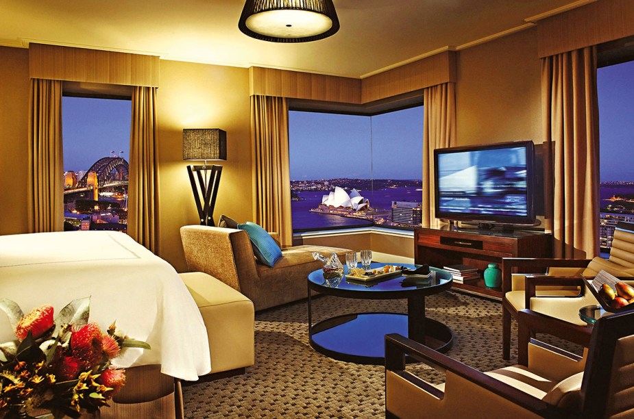 A TV da Junior Suite do <a href="https://www.booking.com/hotel/au/four-seasons-sydney.pt-br.html?aid=332455&sid=d98f25c4d6d5f89238aebe98e11a09ba&dest_id=-1603135&dest_type=city&group_adults=2&group_children=0&hapos=1&hpos=1&no_rooms=1&sr_order=popularity&srepoch=1569951938&srpvid=56a97ce059320025&ucfs=1&from=searchresults;highlight_room=#hotelTmpl" target="_blank" rel="noopener"><strong>Four Seasons Sydney</strong></a> pode até ser full HD, ter a maior seleção de canais a cabo ever, som Dolby, o diabo, mas o que de fato emociona, prende e hipnotiza é a vista das janelas para nada menos do que a <a href="https://viagemeturismo.abril.com.br/atracao/sydney-opera-house/" target="_blank" rel="noopener">Ópera</a> e a ponte Harbour, dois supercartões-postais da <a href="https://viagemeturismo.abril.com.br/paises/australia-2/" target="_blank" rel="noopener">Austrália</a>. O arrebatamento é tamanho que você até esquece que a mobília dos quartos está um pouco cansada e que o wi-fi é pago.