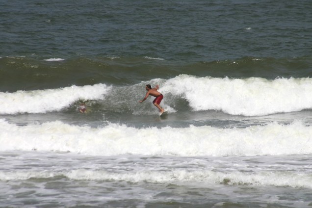 Surfista na Praia do Rezende, que tem pequena faixa de areia e é cercada por coqueiros