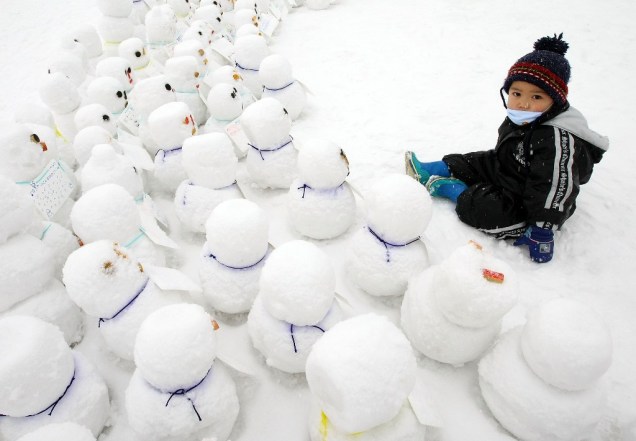 Criança brincando junto a bonecos de neve no Festival da Neve de Sapporo, no norte do Japão