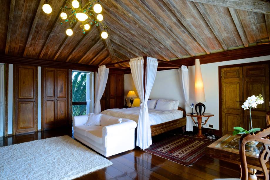 Dos 6 quartos, 5 são suítes – acima, a cama com dossel, o assoalho e o teto de madeira patinada dão certa sofisticação