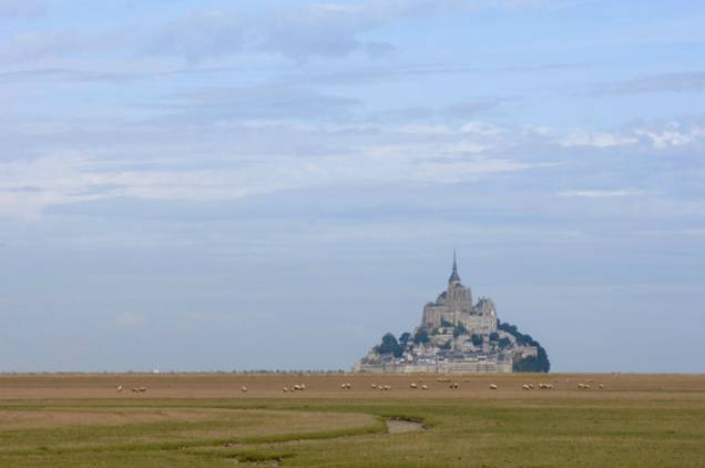 O Mont Saint-Michel em época de maré baixa; a Abadia construída sobre o ponto mais alto do rochedo de granito é a principal atração do local