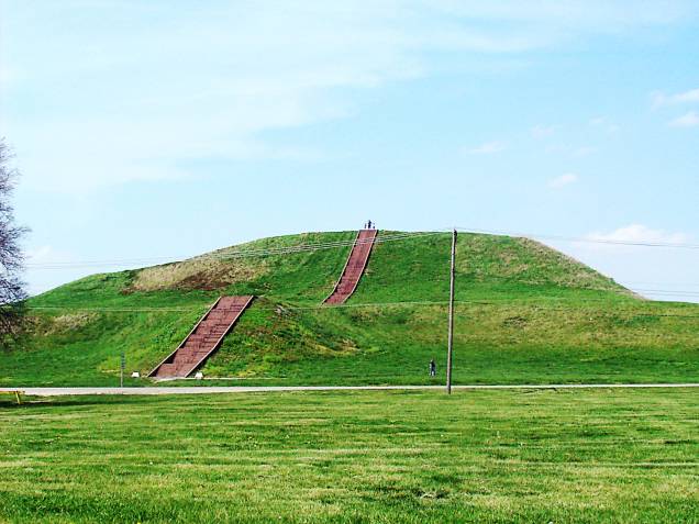 <strong>14. Monks Mound – Cahokia Mounds - EUA </strong>Sim, nos EUA também existem pirâmides! Localizada em Illinois, perto da cidade de St. Louis, esta da foto é apenas um dos mais de 80 edifícios escavados no Sítio Arqueológico Cahokia Mounds. Cahokia era o maior e mais influente assentamento urbano da região do rio Mississipi, que começou há mais de 1.500 anos. É considerado o maior e mais complexo sítio arqueológico a norte das cidades pré-colombianas no México. A Monks Mound tem 30m de altura e uma base de 291m de cada lado (a mesma base da pirâmide de Gizé, no Egito, porém bem mais baixa). Ela foi construída de terra, argila e madeira e possui uma rampa de acesso até seu topo. Porque os materiais utilizados são instáveis, a pirâmide sofreu diversos deslizamentos que fizeram com que sua base ficasse tão ampla já durante a construção.
