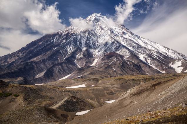 <strong>Koryaksky, Península de Kamchatka</strong> O vulcão marca presença mesmo visto de longe. O formato bem regular, simétrico e elegante de sua encosta agrega ainda mais a sua beleza de 3 mil metros de altura. A erosão natural formou vales em que a neve se acumula e forma belos desenhos em sua superfície. Ele ainda faz parte do famoso Círculo de fogo do Pacífico, uma região onde se localiza vários vulcões e placas tectônicas que frequentemente se chocam e produzem terremotos <strong>Koryaksky, Península de Kamchatka</strong> O vulcão marca presença mesmo visto de longe. O formato bem regular, simétrico e elegante de sua encosta agrega ainda mais a sua beleza de 3 mil metros de altura. A erosão natural formou vales em que a neve se acumula e forma belos desenhos em sua superfície. Ele ainda faz parte do famoso Círculo de fogo do Pacífico, uma região onde se localiza vários vulcões e placas tectônicas que frequentemente se chocam e produzem terremotos