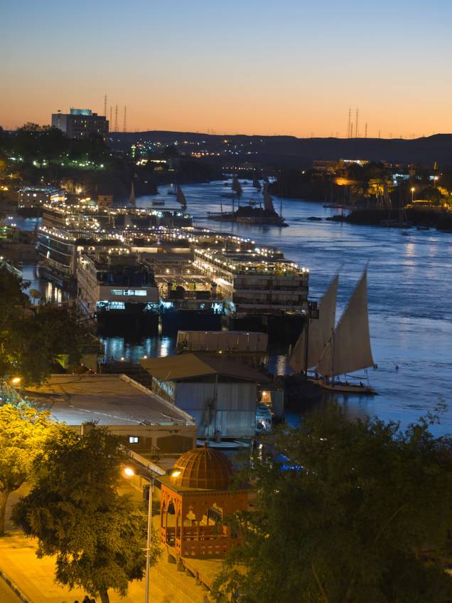 Pôr-do-sol em Aswan, com feluccas e dahabiyas, embarcações de cruzeiro, ancoradas ao longo do rio Nilo Pôr-do-sol em Aswan, com feluccas e dahabiyas, embarcações de cruzeiro, ancoradas ao longo do rio Nilo
