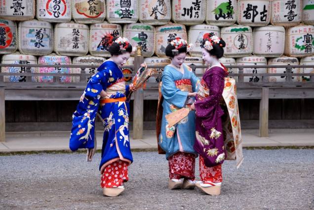 Aprendizes de geisha, conhecidas como maiko, vestem-se com seus coloridos kimonos no santuário Matsuo Taisha, em Kyoto. Ao fundo, tambores de sakê utilizados como oferendas.