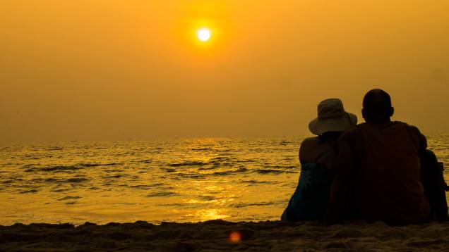 Casal assiste ao pôr do sol em praia de Goa, na Índia Casal assiste ao pôr do sol em praia de Goa, na Índia