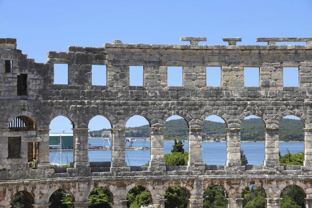 Vista do porto de Pula a partir das ruínas do anfiteatro; apesar de ser menor do que o Coliseu de Roma, a construção é bem conservada. Ainda é possível ver os ganchos que prendiam os dosséis usados na época para proteger os espectadores do sol