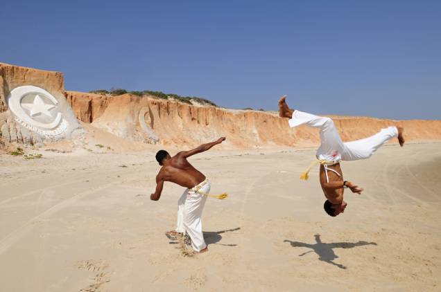 Capoeiristas na praia do centrinho de Canoa Quebrada. Ao fundo, o símbolo do destino esculpido na pedra