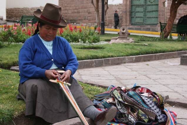 Com roupas típicas peruanas, mulher faz artesanato na calçada de Cusco