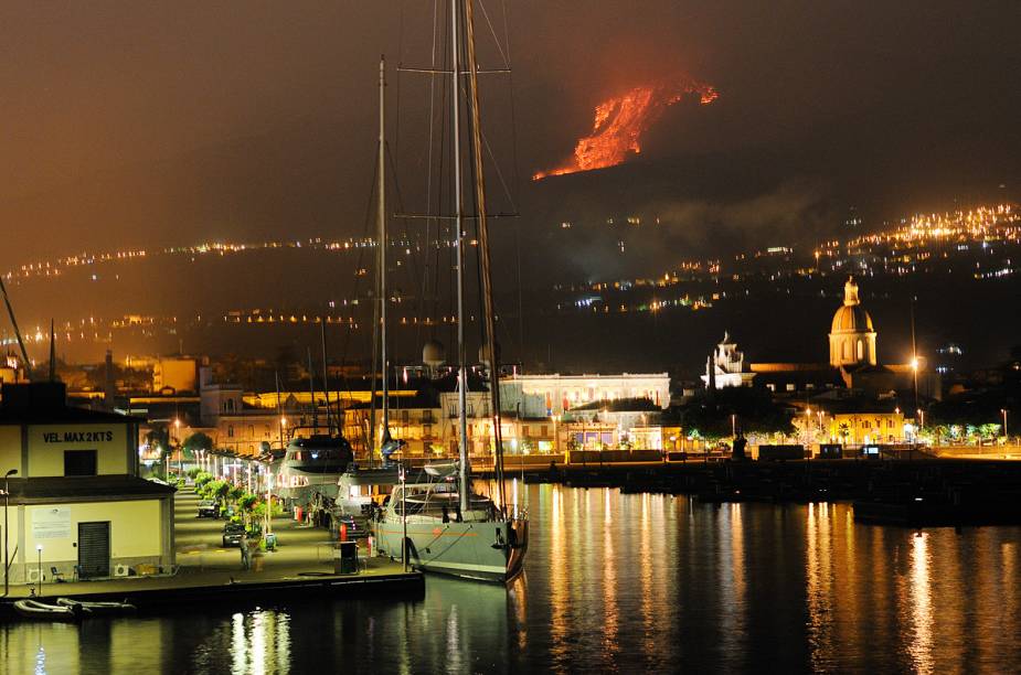 Em foto de 30 de julho de 2011, o vulcão Etna irrompe em uma erupção (ao fundo), enquanto a cidade de Catânia entra em estado de alerta