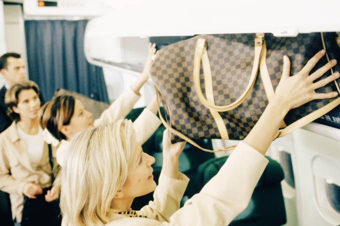 Mulher loira pega a bagagem de mão no compartimento de bagagem da cabine de avião após o pouso