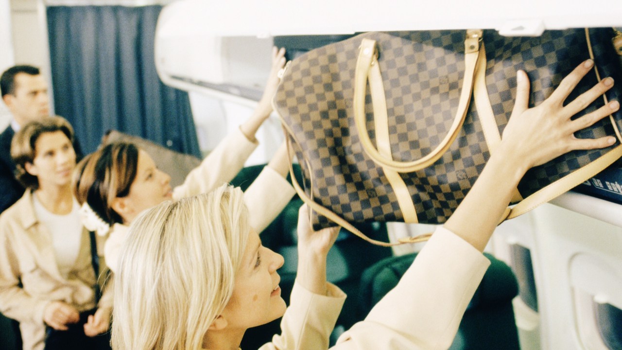 Mulher loira pega a bagagem de mão no compartimento de bagagem da cabine de avião após o pouso