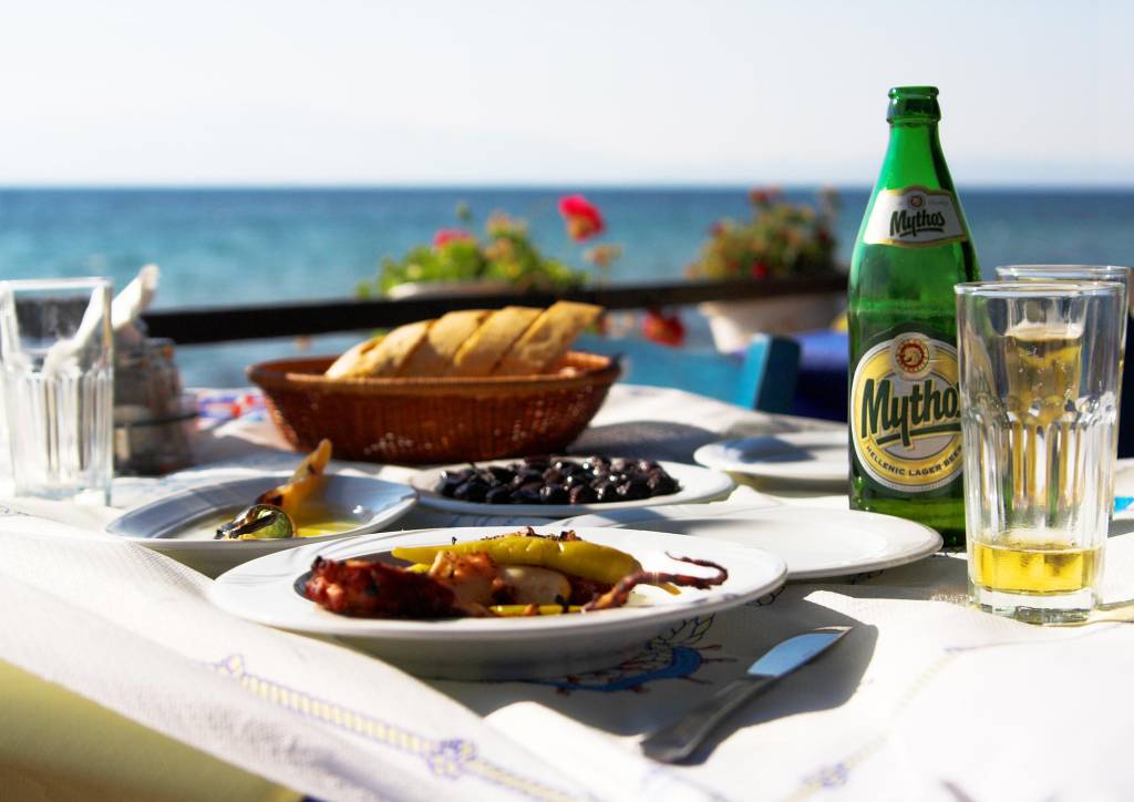 Mesa com polvo grelhado, fava, cerveja Mythos e comidas gregas