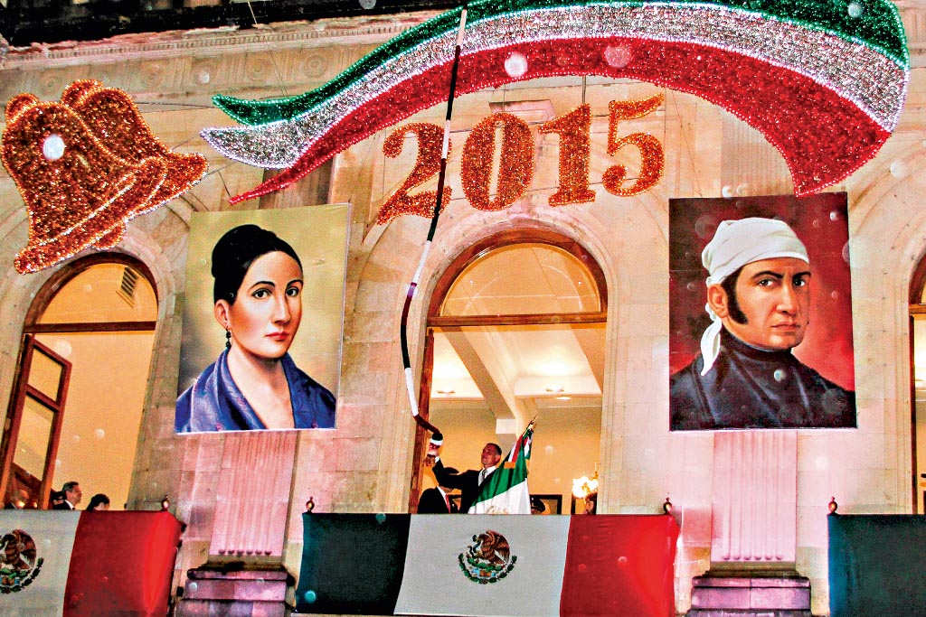 Em uma varanda de um edifício decorado com bandeiras e símbolos com as cores do México, um homem de autoridade no centro, segurando uma bandeira