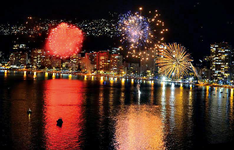 A cena mostra a cidade de Acapulco em frente ao mar, com fogos de artifício em abundância estourando por cima da praia
