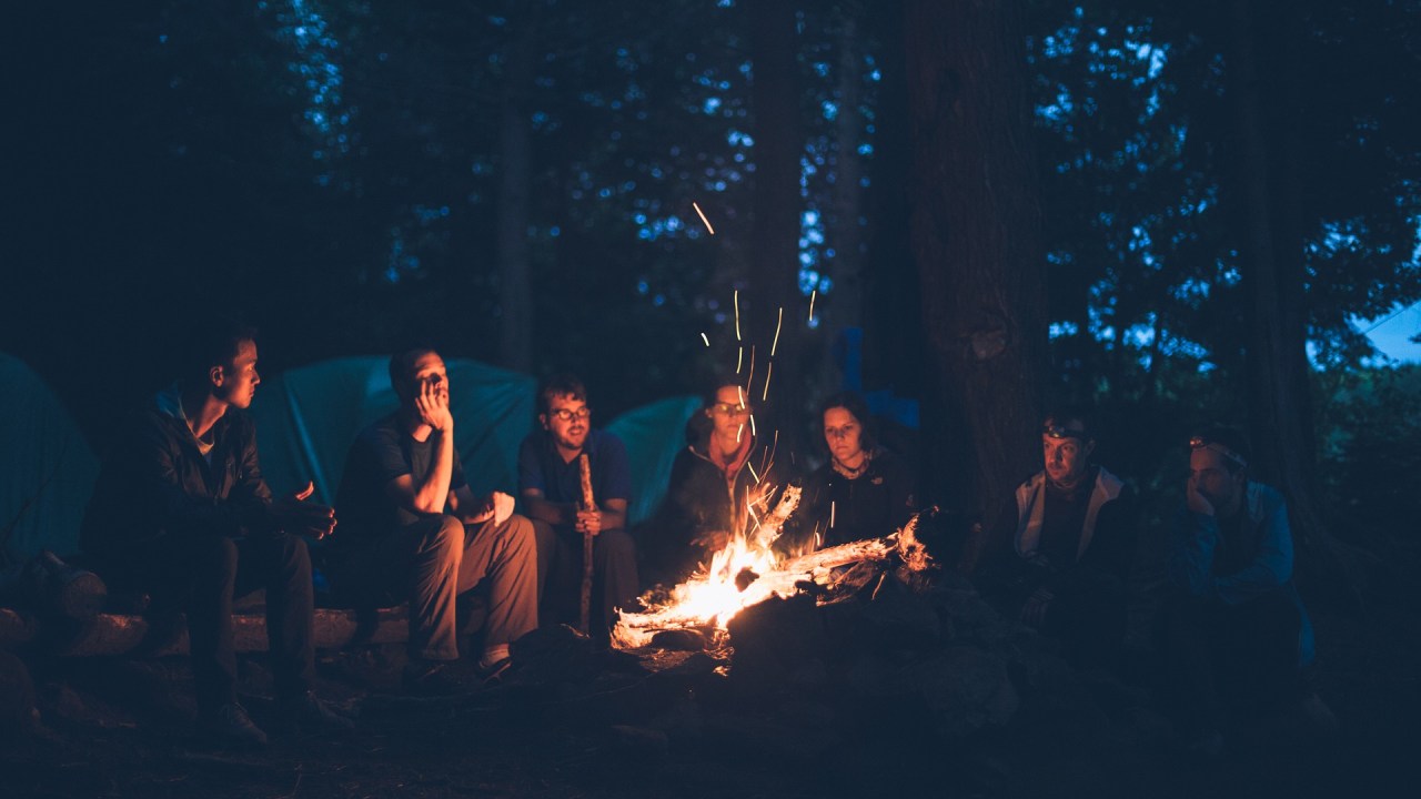 Turma de amigos acampando e sentados em volta da fogueira, à noite