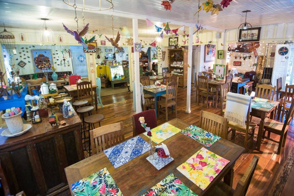 Ambiente do restaurante Empório com Arte, em Foz do Iguaçu (PR), com mesas de madeira e retalhos coloridos