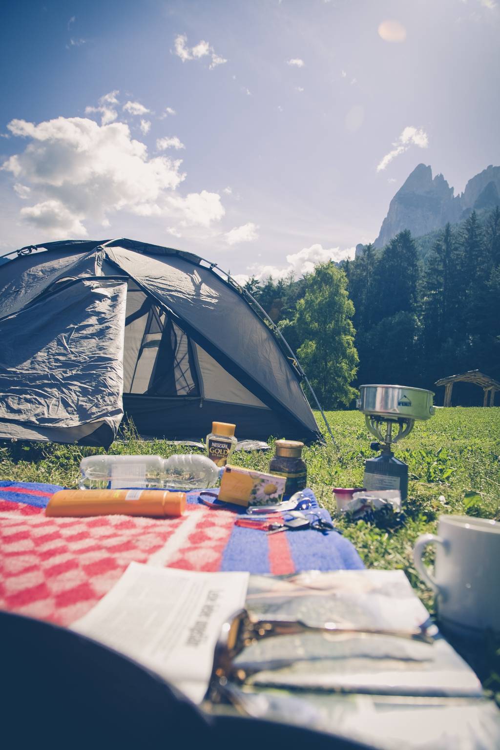 Gramado com barraca de camping, fogareiro e canga em um dia de sol num campo aberto