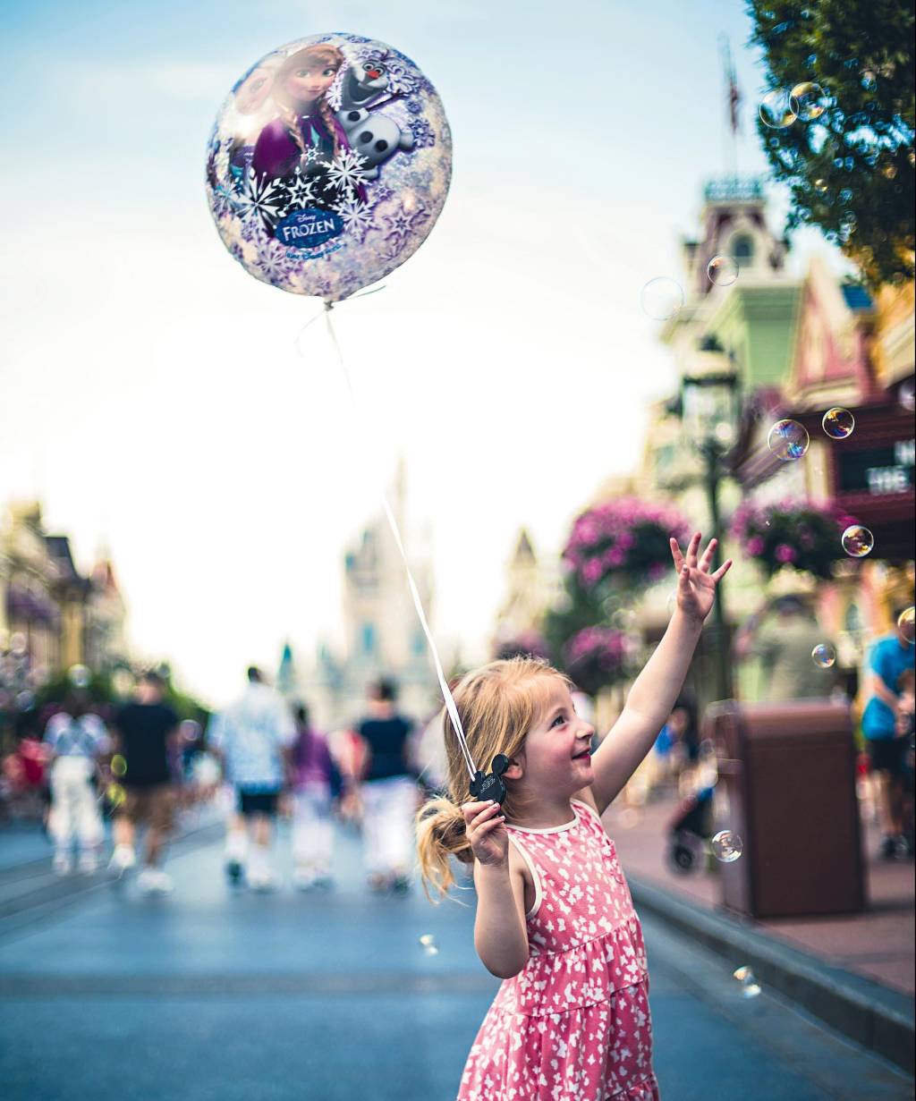 Menina segura um balão com uma imagem do filme "Frozen", enquanto tenta agarrar bolhas de sabão
