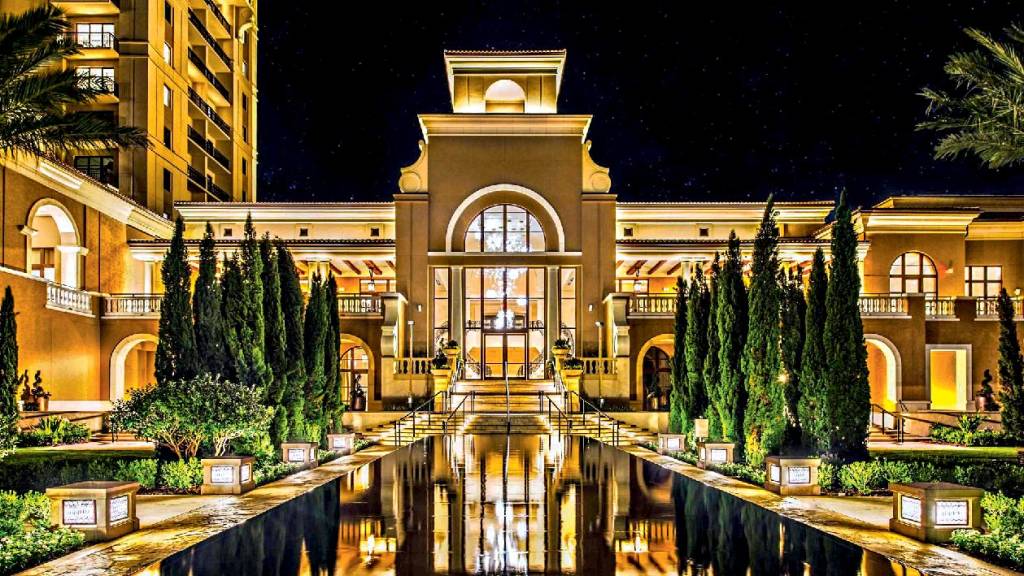 Uma grande piscina reflete a iluminação de um prédio luxuoso, que abriga o Four Seasons Orlando