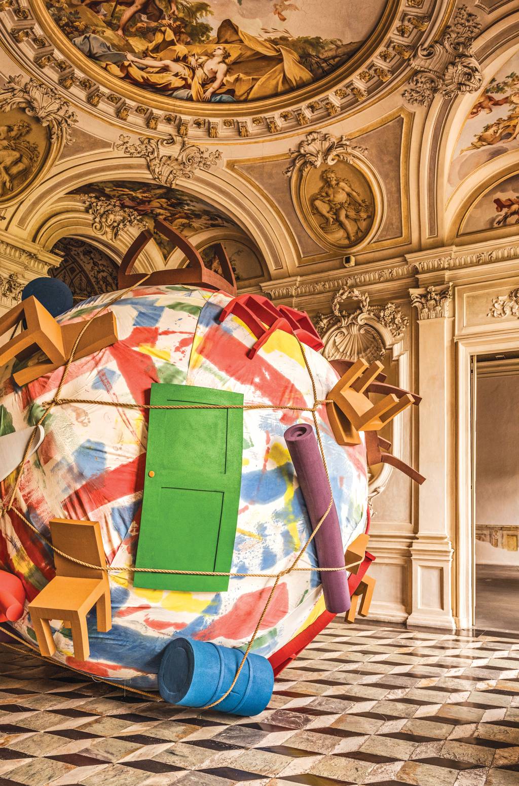 Portas, cadeiras, esteiras e outros objetos do cotidiano estão amarrados com uma corda a uma bola gigante, que representa o planeta Terra. A escultura está dentro de uma sala ricamente adornadas com entalhes e pinturas que remontam à cultura da Grécia Antiga