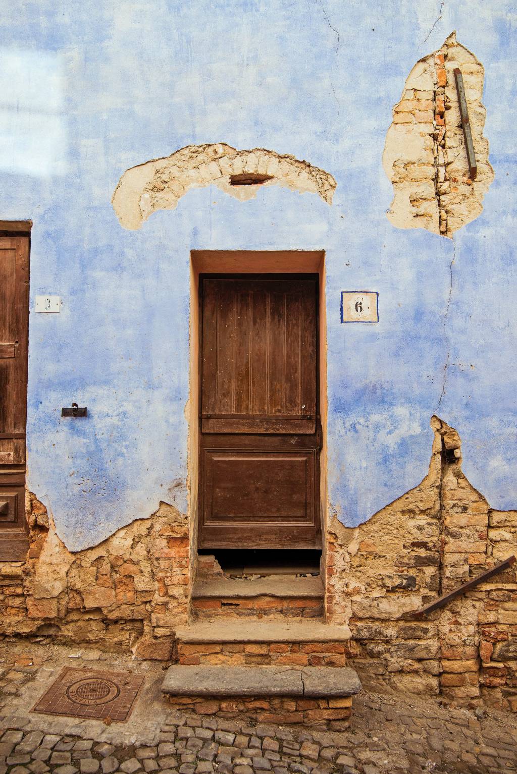 Pequena porta de madeira, incrustada em uma parede com rachaduras e tijolos à mostra