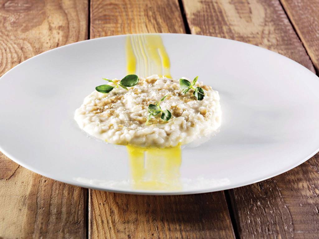 Risoto do restaurante La Gallina, Piemonte, Itália Risoto cremoso sobre prato, em uma mesa de madeira