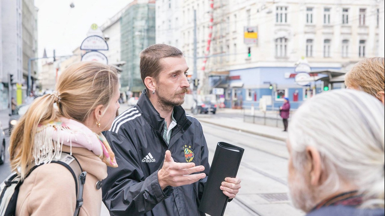 Morador de rua explica a cidade de Viena para turistas participantes do Shades Tour