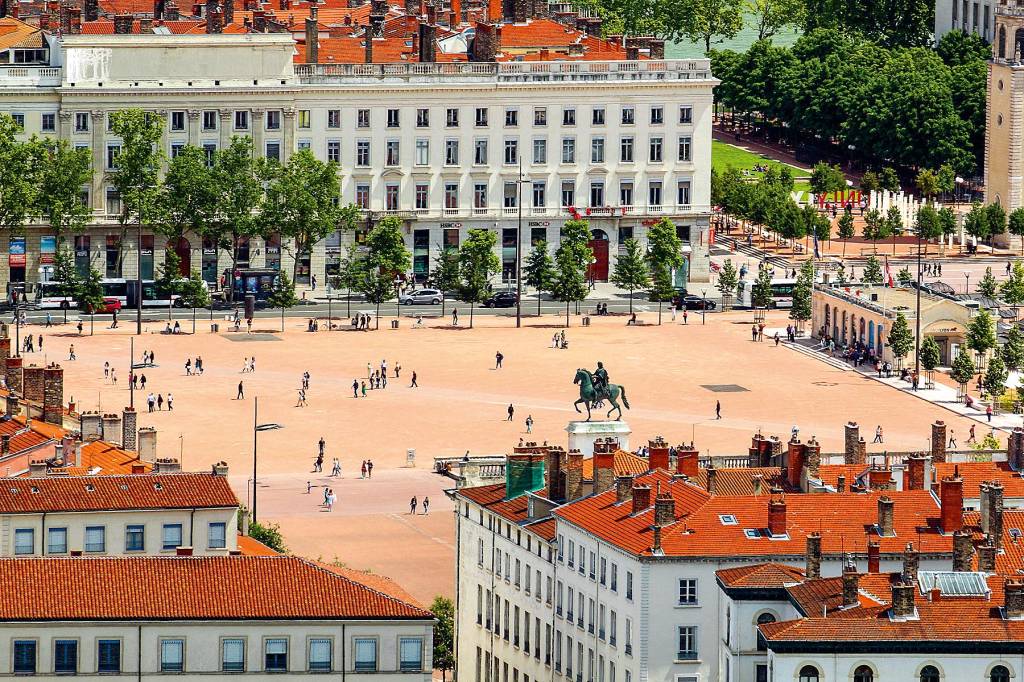 Uma praça aberta e com poucas árvores ou terra, no meio de prédios franceses