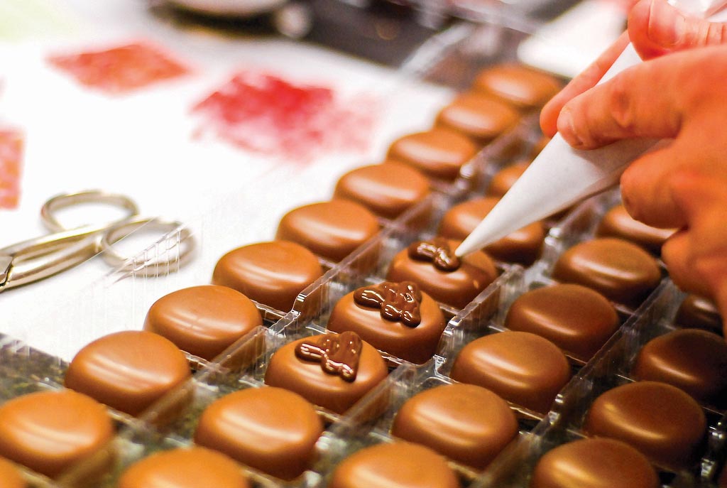 Um confeiteiro aplica coberturas de chocolate em cima de bonbons