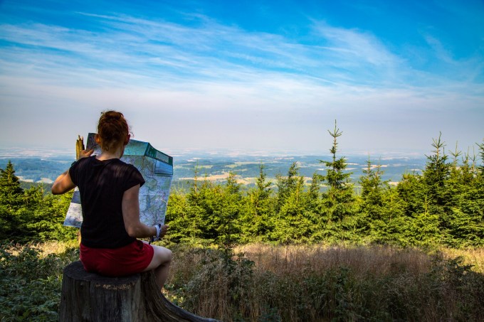 Mulher turista lê mapa de cidade com cenário de árvores ao fundo, no horizonte