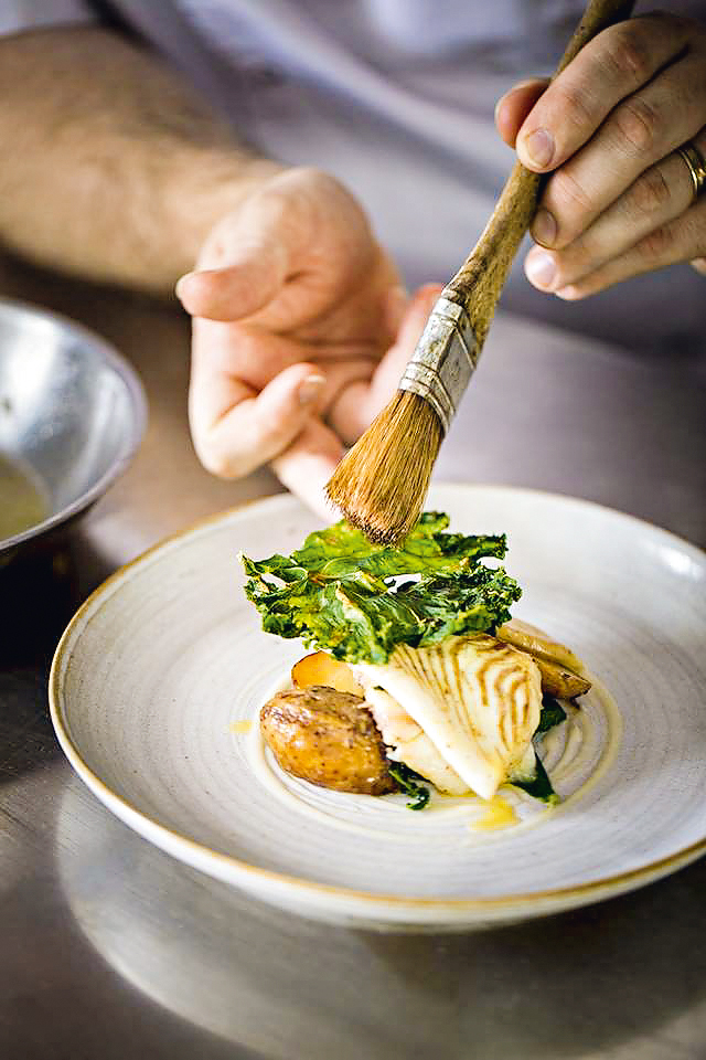 Prato sofisticado de batata e frango sendo finalizado com uma pincelada do cozinheiro