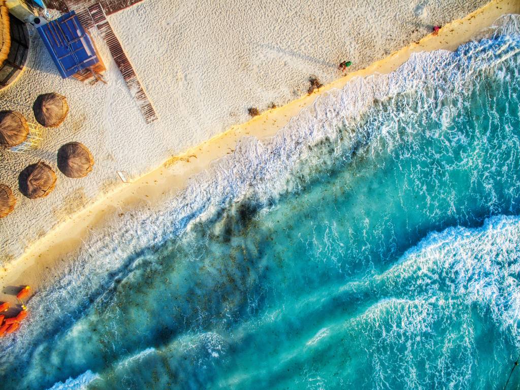 Vista aérea do praia, com metade da foto encoberta por ondas suaves do mar azul