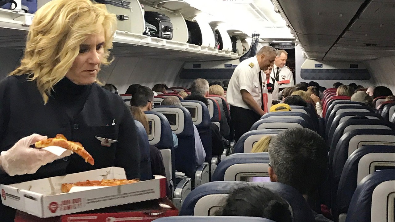 Aeromoça da Delta Air Lines distribui pizzas para passageiros dentro de avião que esperavam pelo embarque nos Estados Unidos
