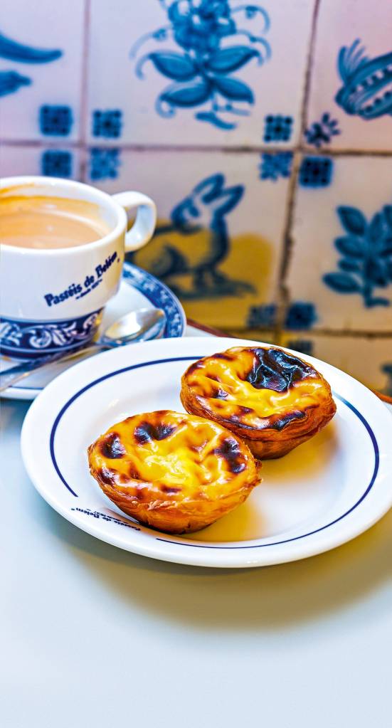 Dois pastéis de Belém em ambiente típico português, com prataria e azulejo simples