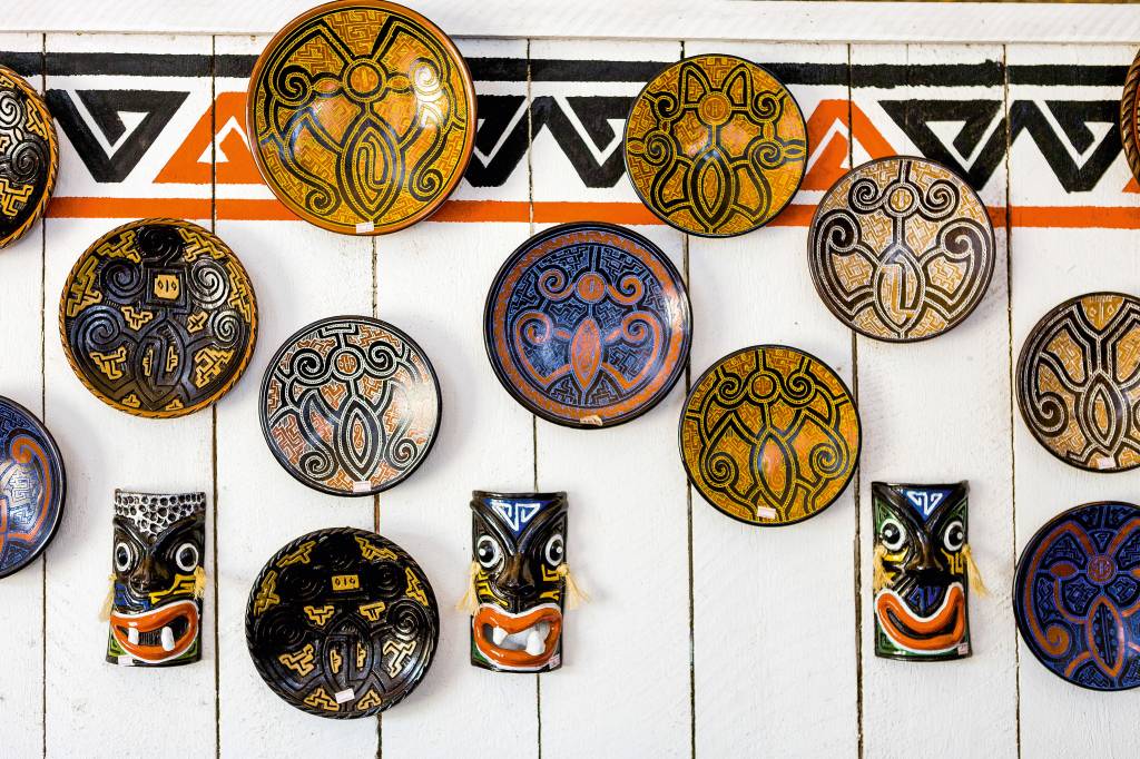 Pratos e máscaras artesanais com desenhos diferentes e tribais penduradas em uma parede